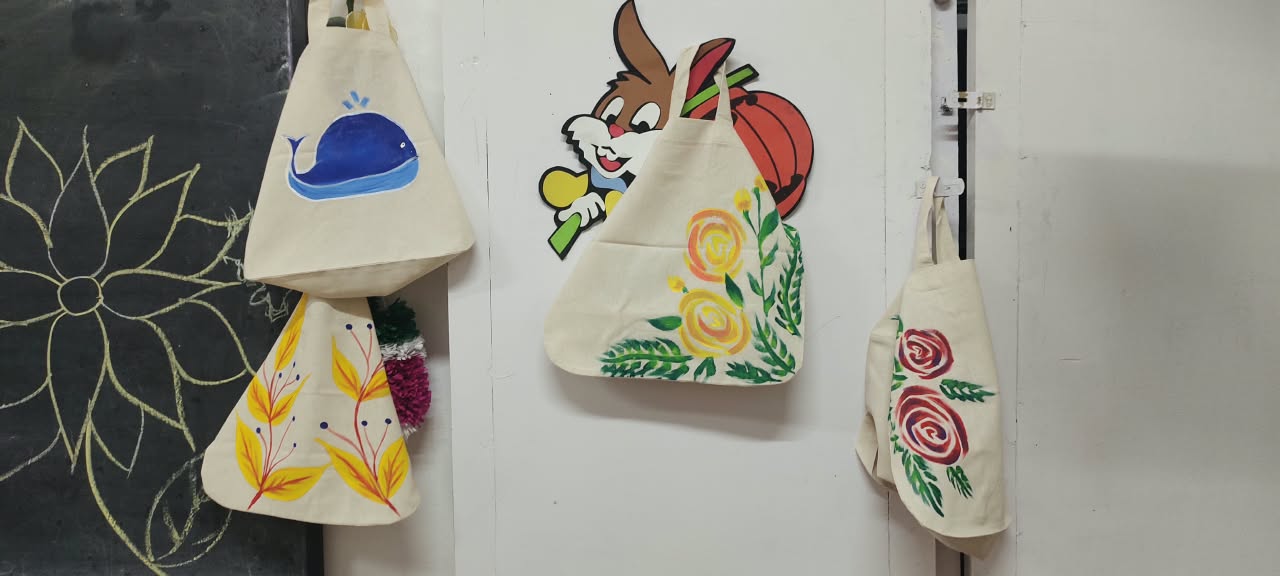 Four hand-painted canvas tote bags with a whale, autumn leaves, roses and flowers, hanging up to dry