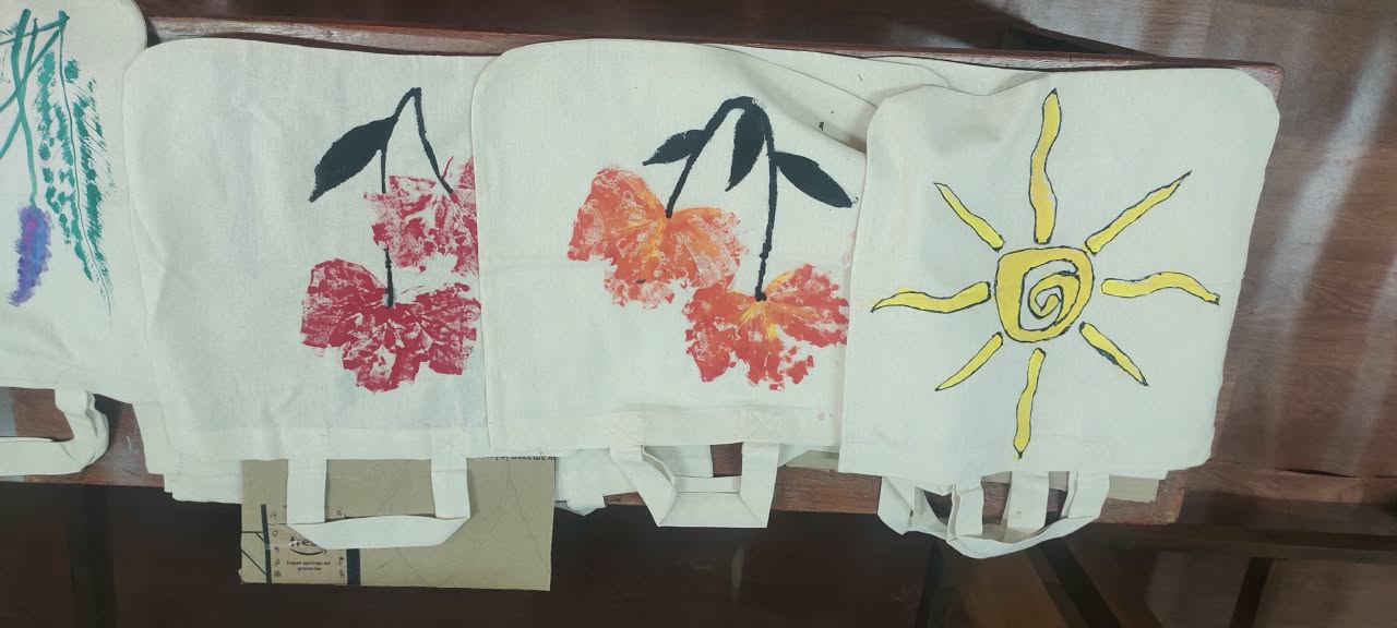 Tote bags painted with leaf prints, cherries and a sun design laid out to dry
