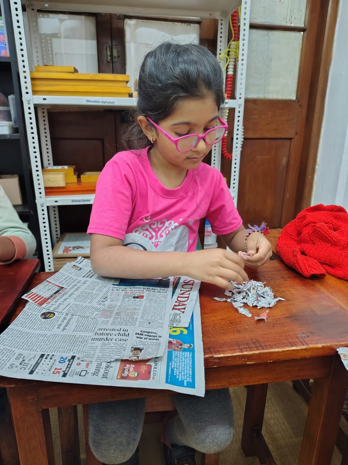 A Grade 1 child in a pink shirt tearing old newspaper into small pieces for handmade paper at bms