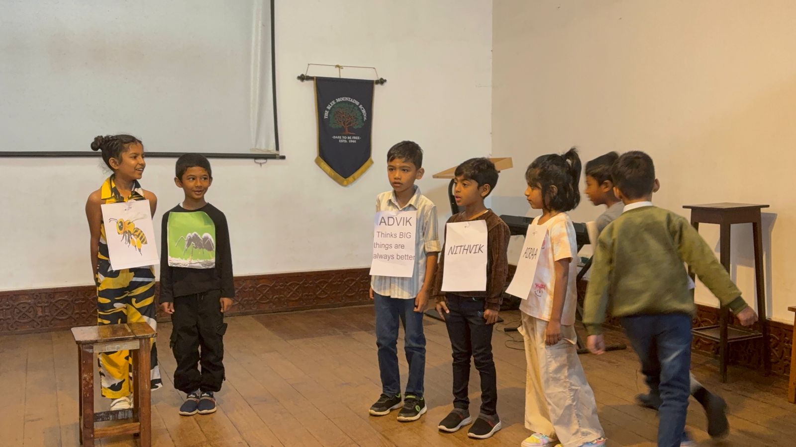 A student dressed as a bee joins alongside the ant as more classmates arrive on stage