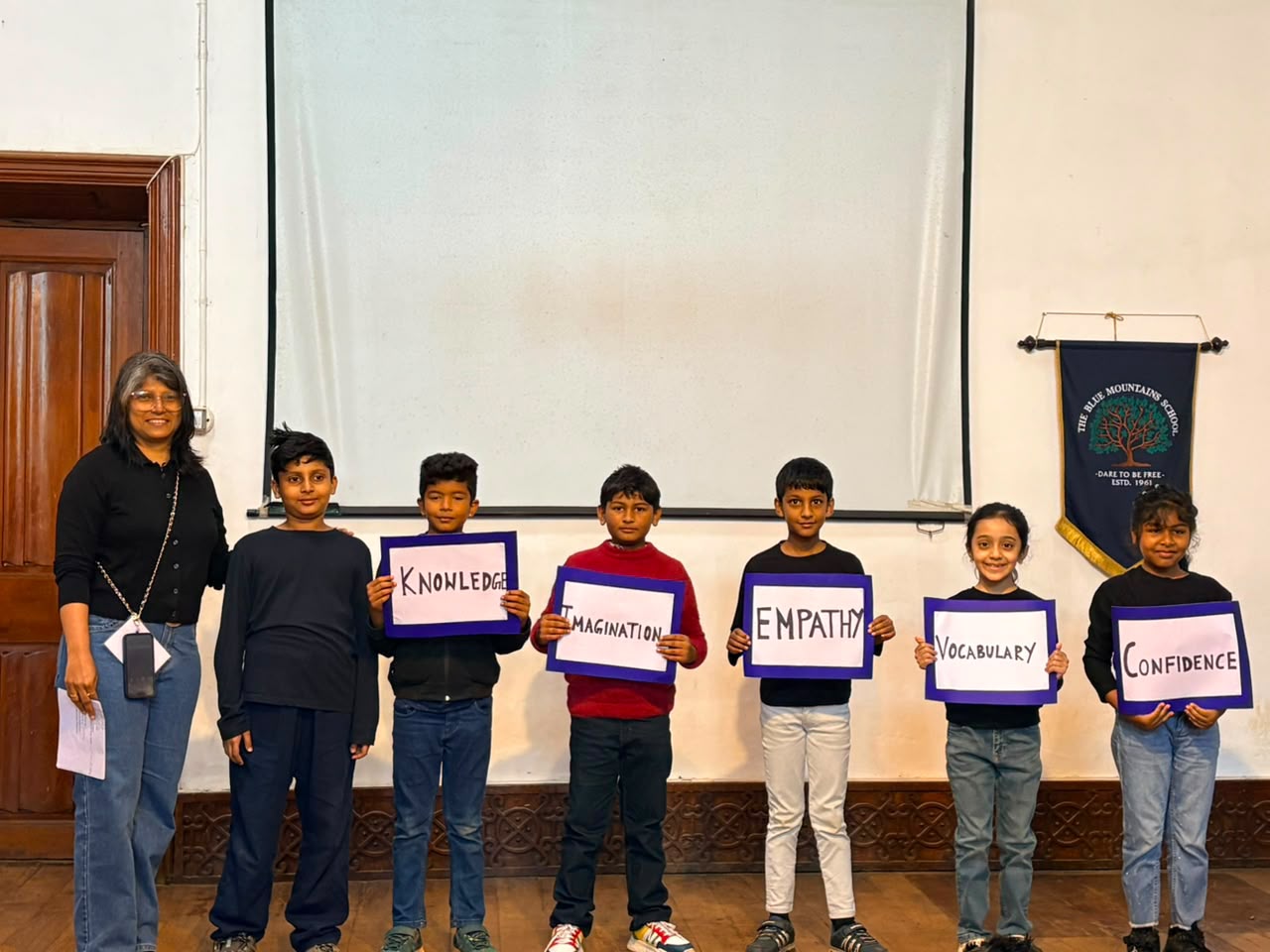 Grade 3 students and their teacher holding cards reading Knowledge, Imagination, Empathy, Vocabulary and Confidence