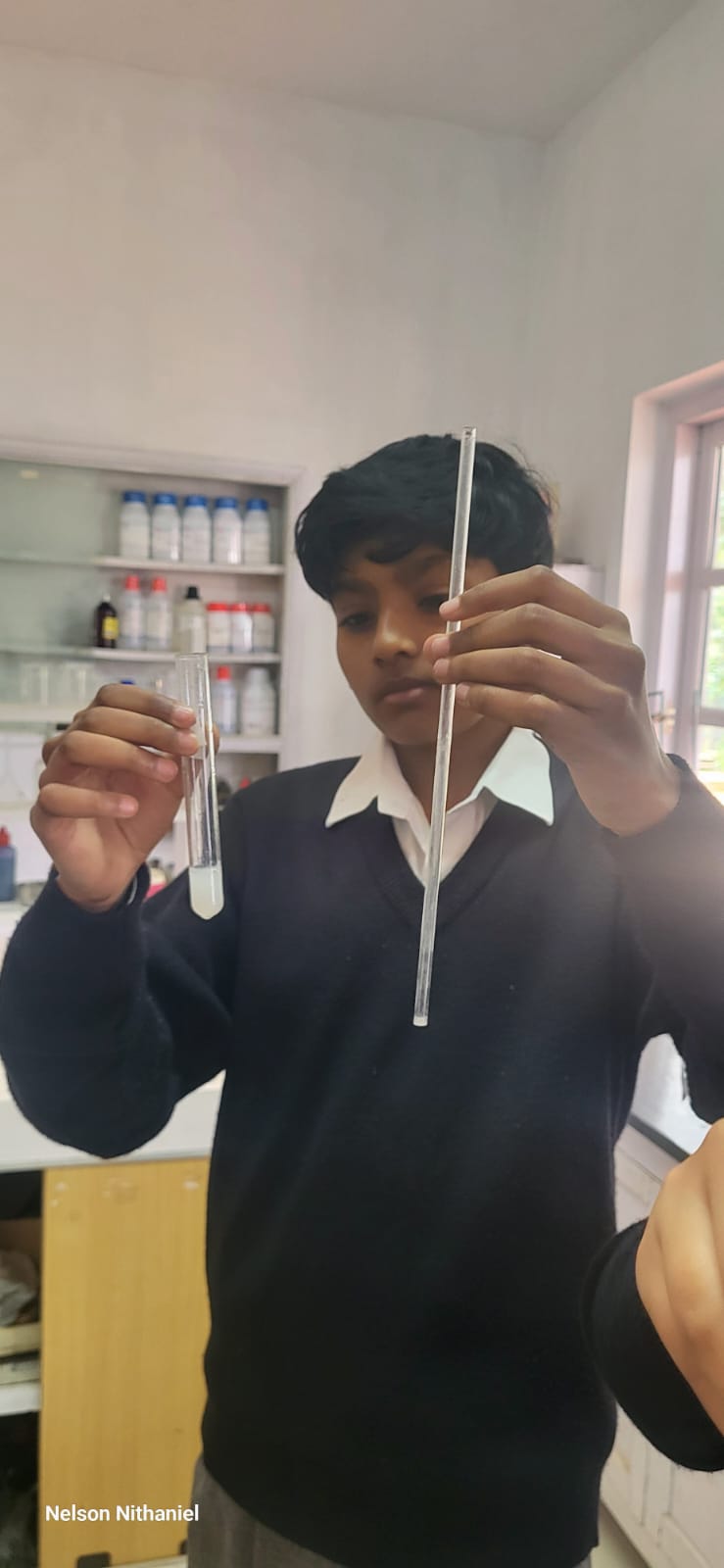 A student holding a straw and a test tube of milky lime water