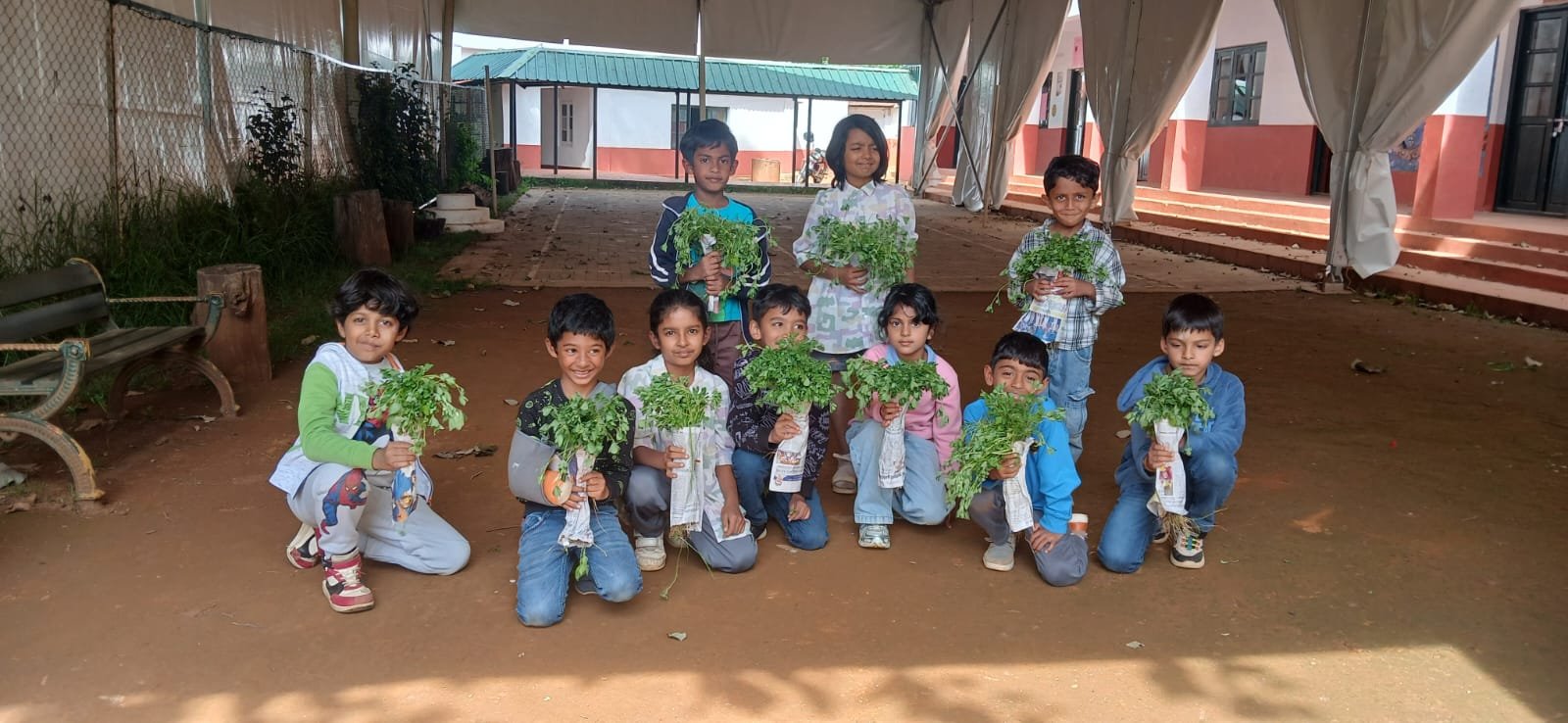 Students holding freshly harvested bunches of methi in the school garden