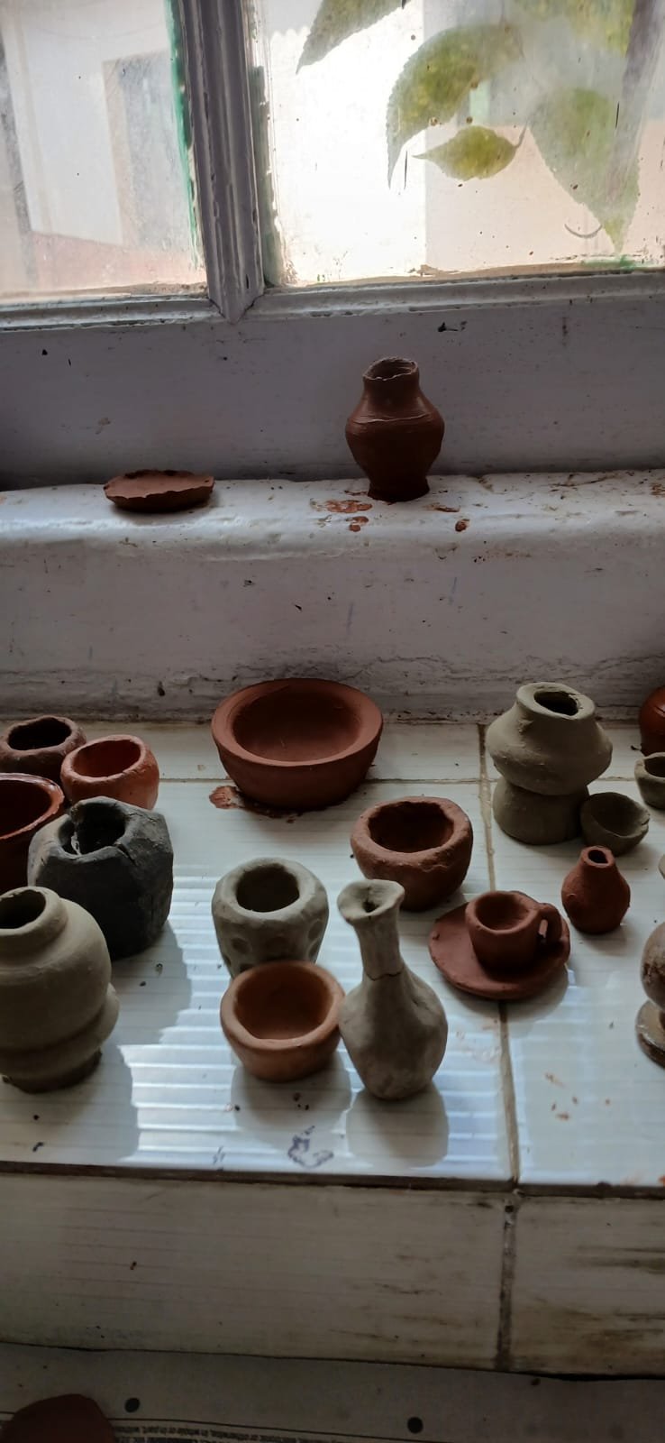 Finished clay pots and bowls drying on the windowsill